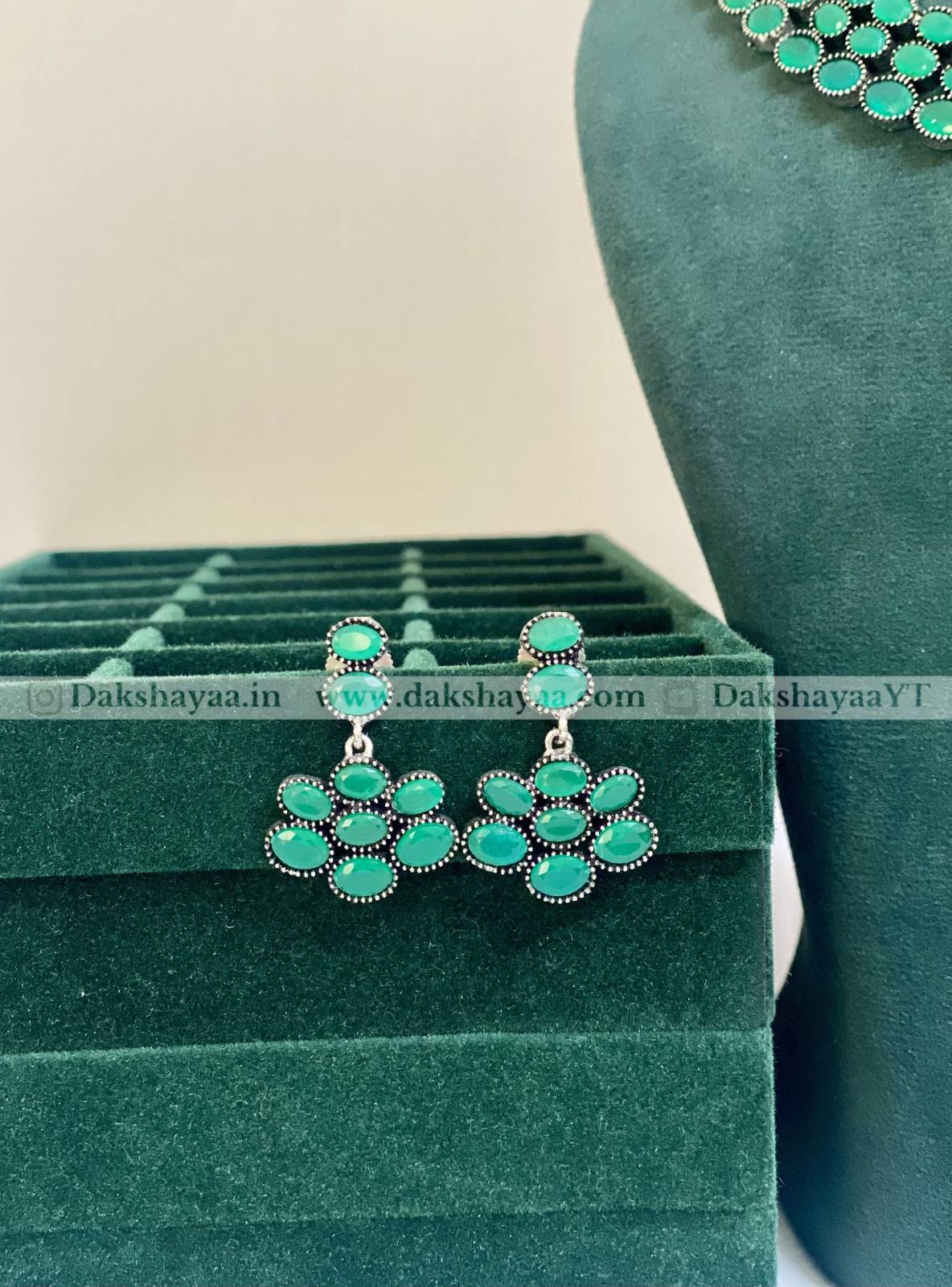 Green earrings on a green jewelry display stand with a blurred background