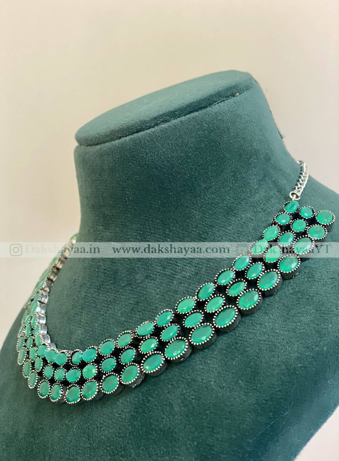 Green beaded necklace on a green velvet stand with a beige background