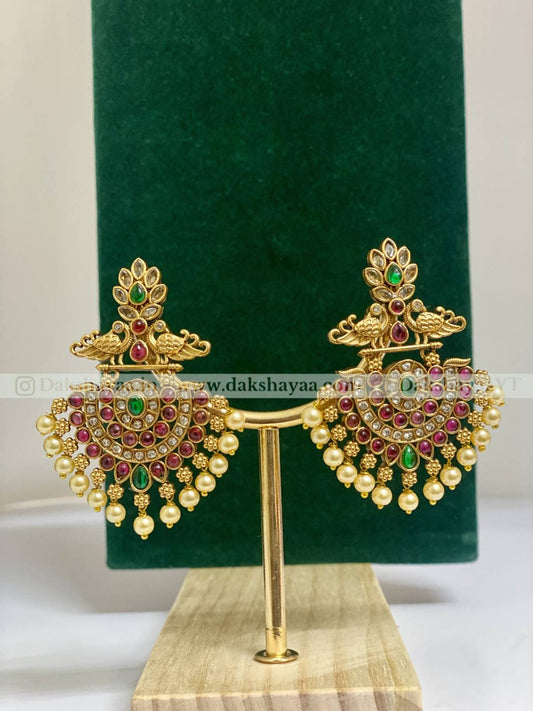 Gold earrings with green and red stones on a green velvet stand