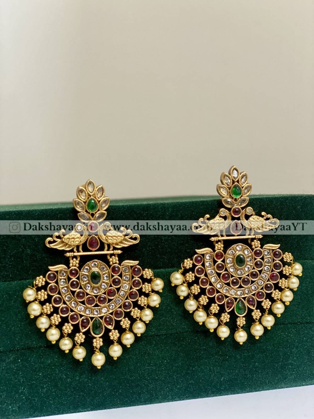 Pair of ornate gold earrings with pearls and gemstones on a green background