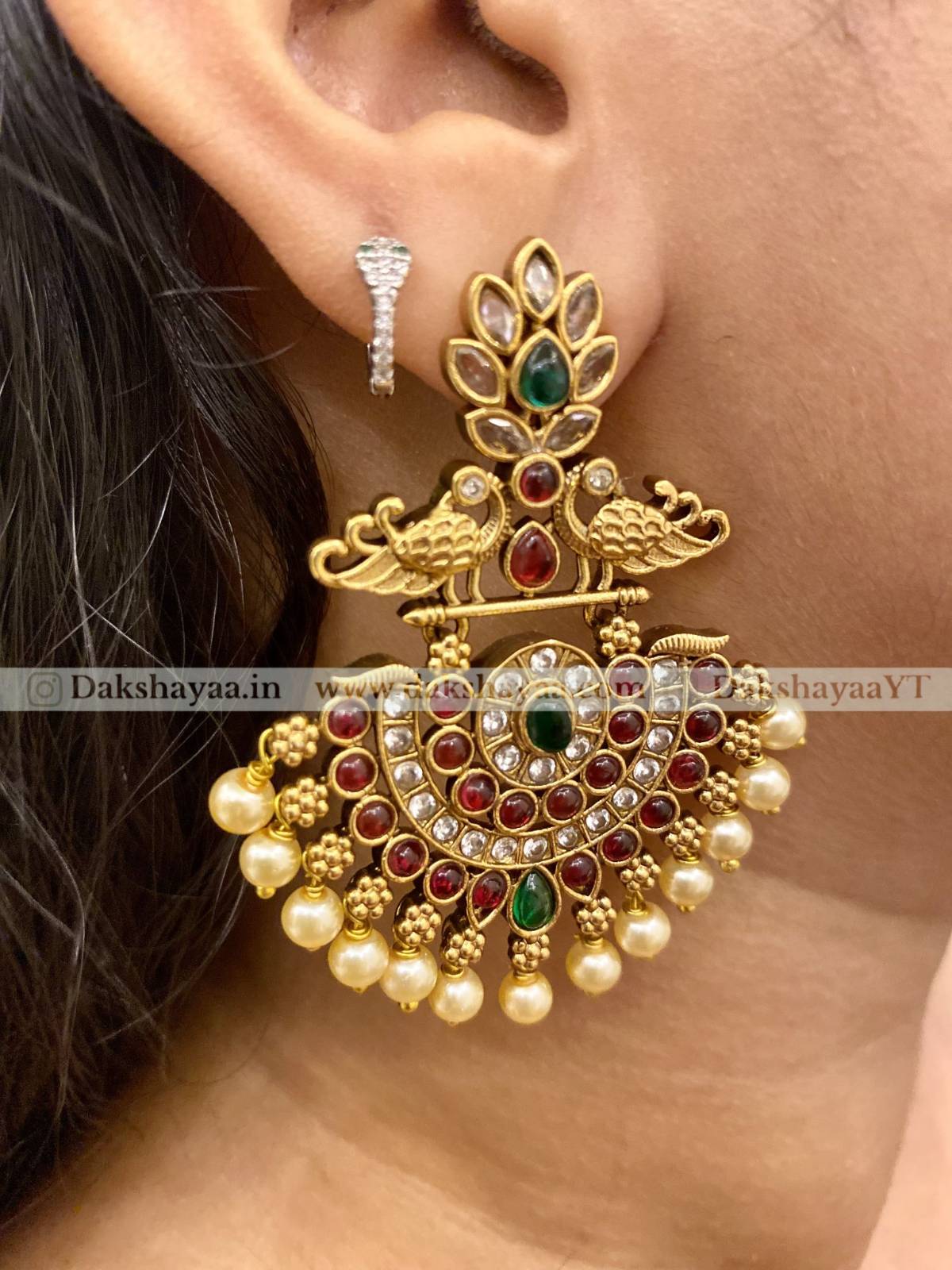 Gold earrings with gemstones and pearls worn by a person