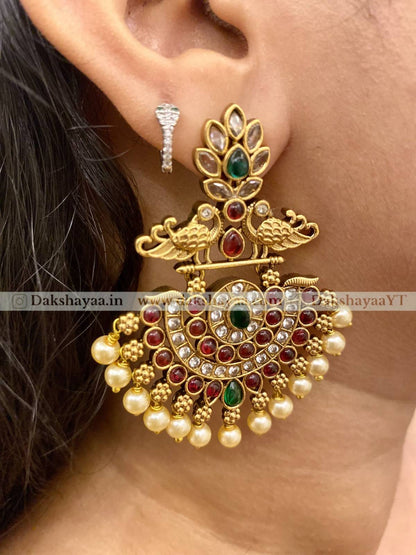 Gold earrings with gemstones and pearls worn by a person