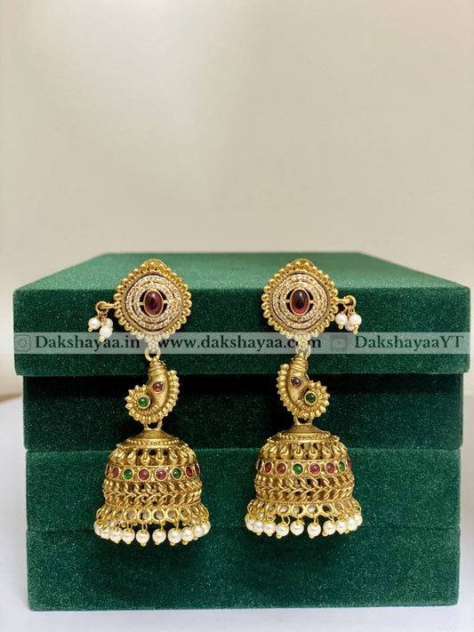Gold jhumka earrings with red and green stones on a green velvet box