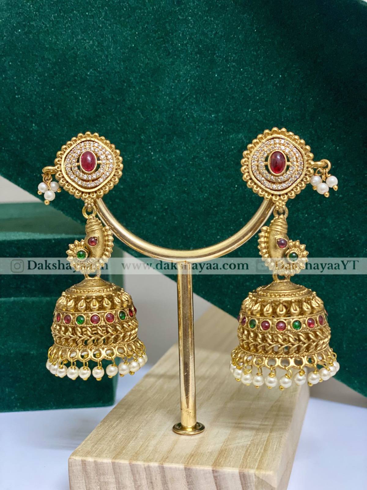 Gold earrings with red and green gemstones on a stand against a green background