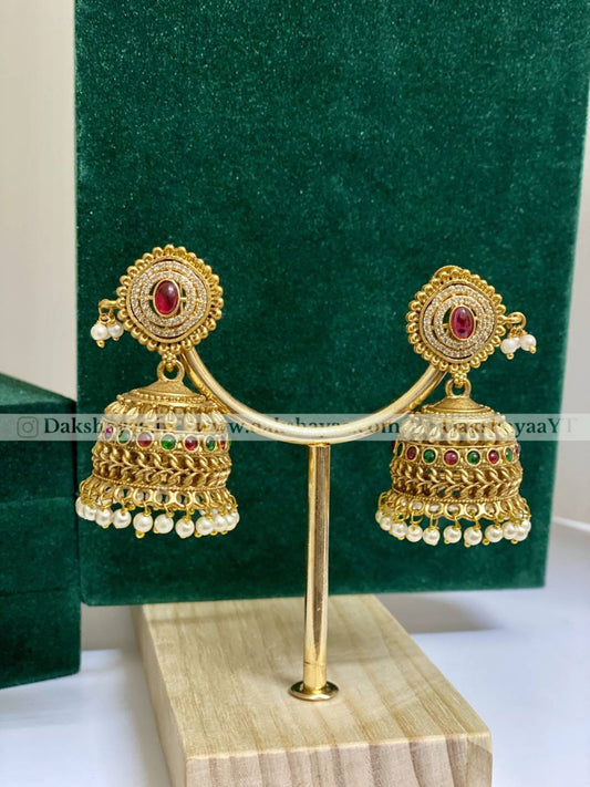 Gold earrings with red and green stones on a green stand