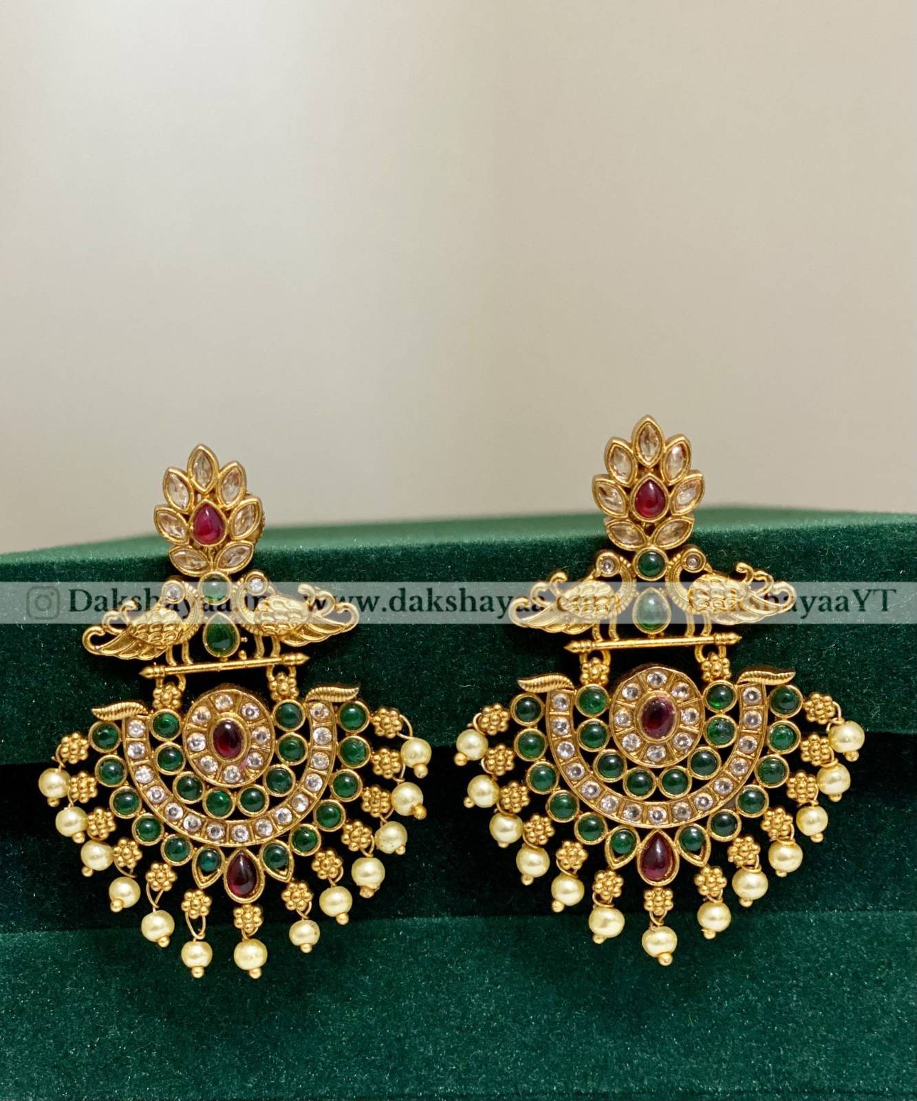 Pair of gold earrings with gemstones on a green cushion