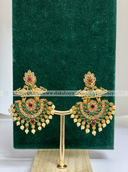 Gold earrings with red and green stones on a green velvet stand