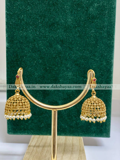 Gold earrings with pearl details on a green stand with 'Dakshayaa' branding.