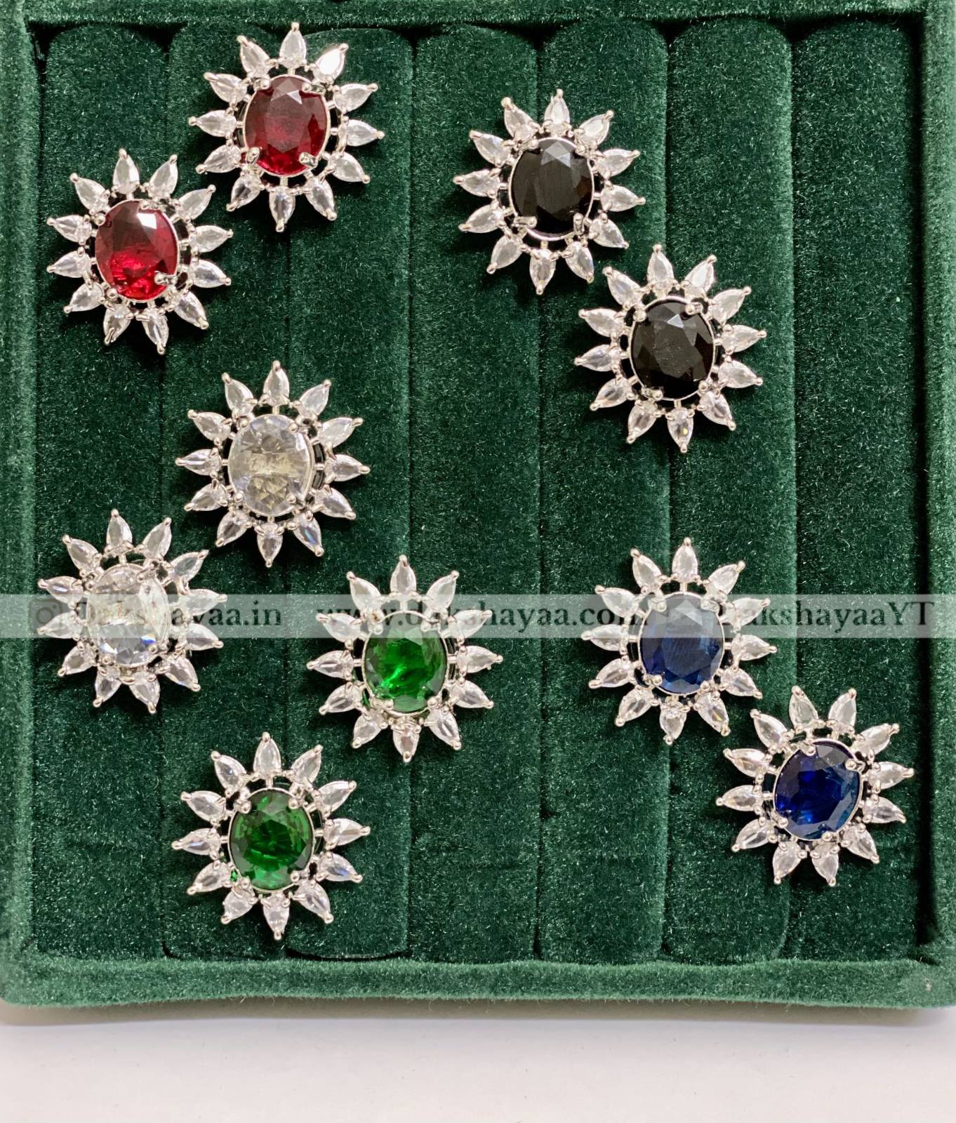 Set of silver flower-shaped earrings with colored gemstones on a green velvet background