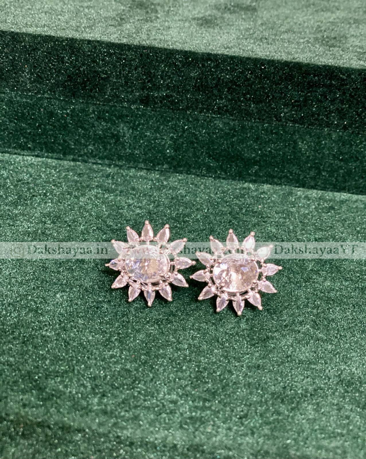 Silver flower-shaped earrings on a green fabric background