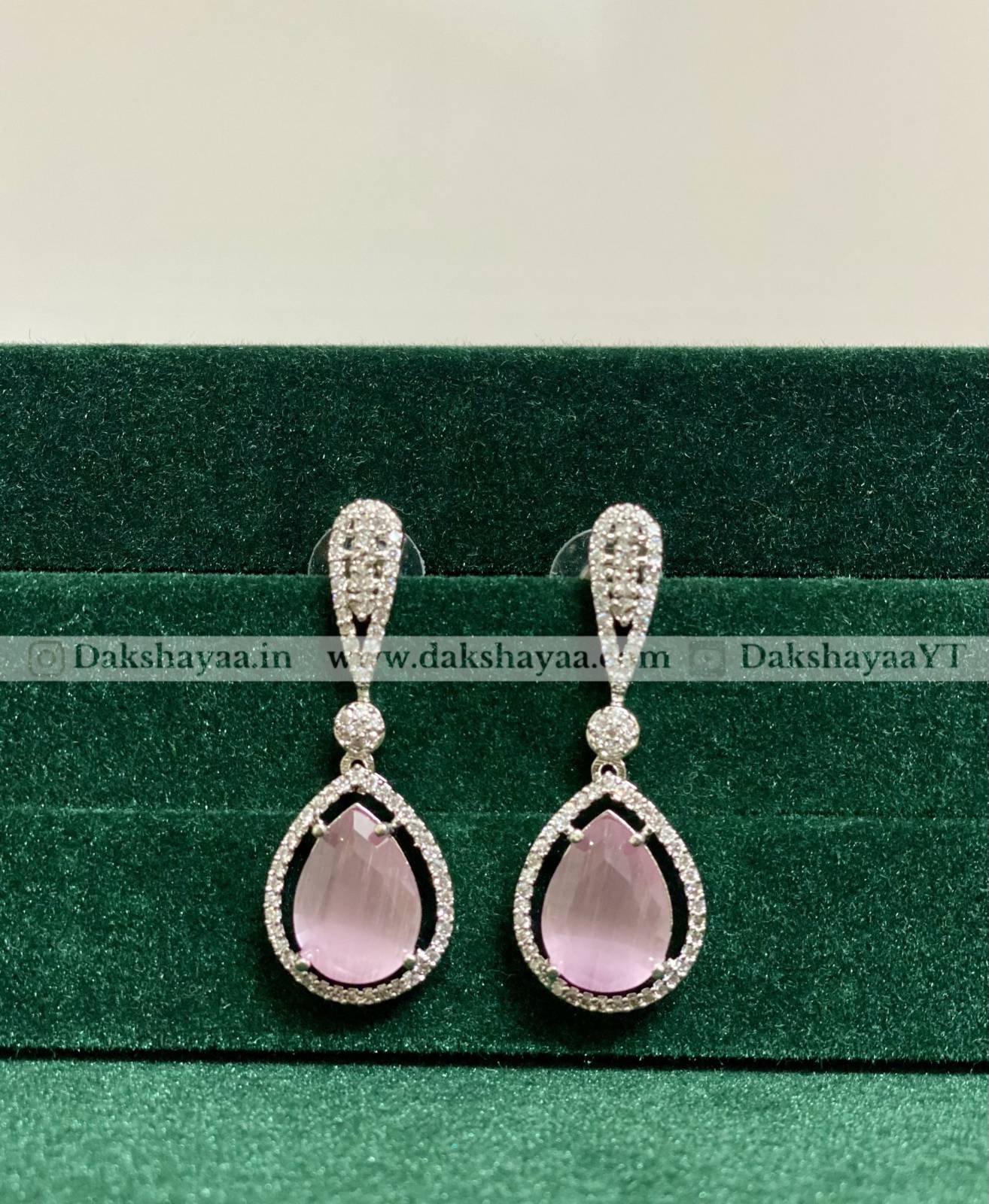 Teardrop-shaped pink gemstone earrings with silver detailing on a green background