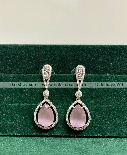 Teardrop-shaped pink gemstone earrings with silver detailing on a green background