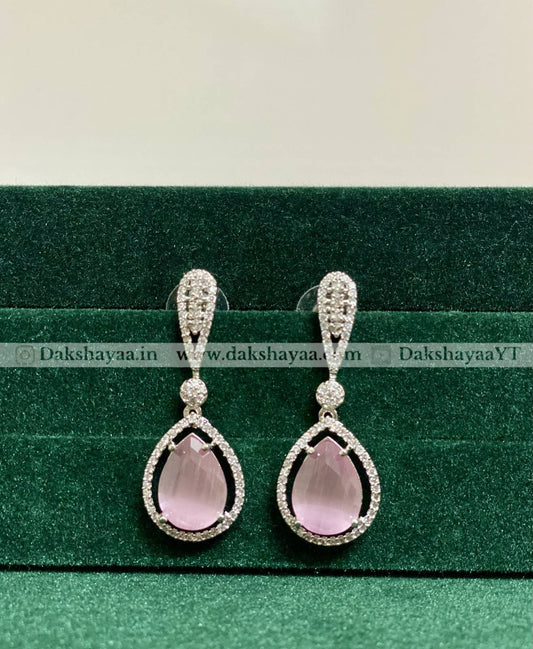Teardrop-shaped pink gemstone earrings with silver detailing on a green background