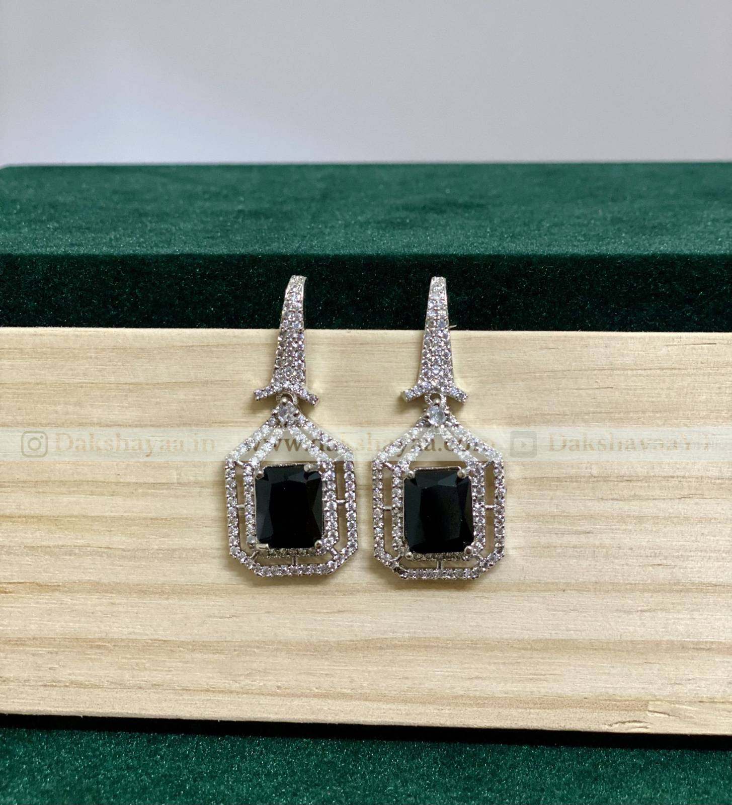 Pair of earrings with black gemstones and silver frames on a wooden surface.