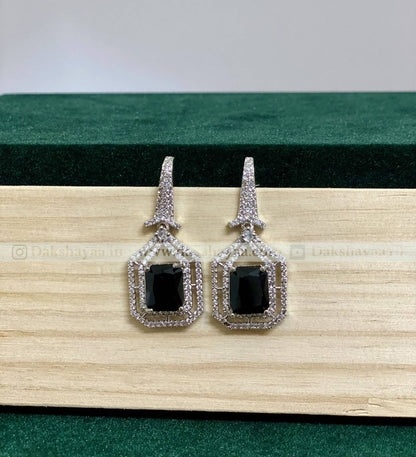 Pair of earrings with black gemstones and silver frames on a wooden surface.