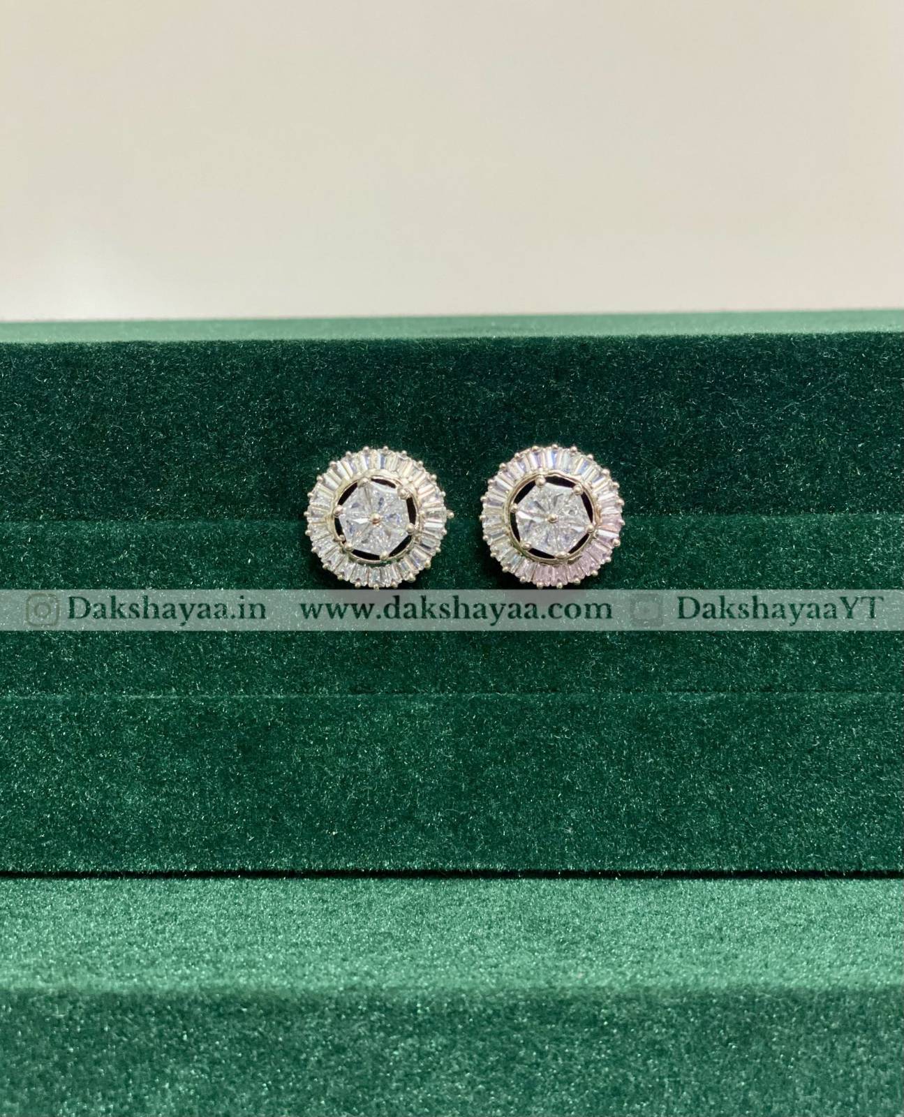 Pair of silver earrings with gemstones on a green velvet stand.