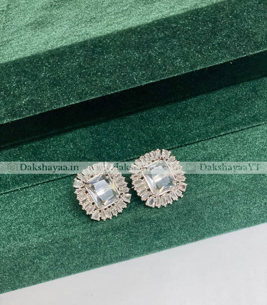 Pair of silver earrings with clear gemstones on a green textured surface