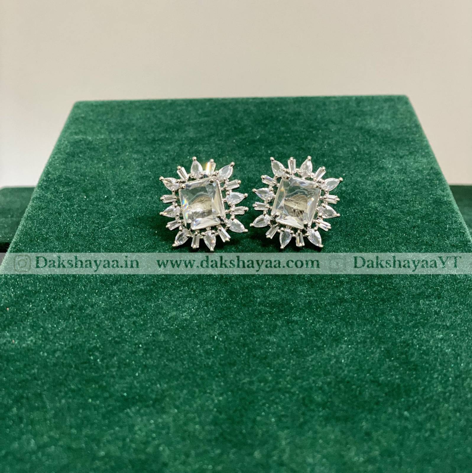 Silver earrings on a green cushion with 'Dakshayaa' branding.