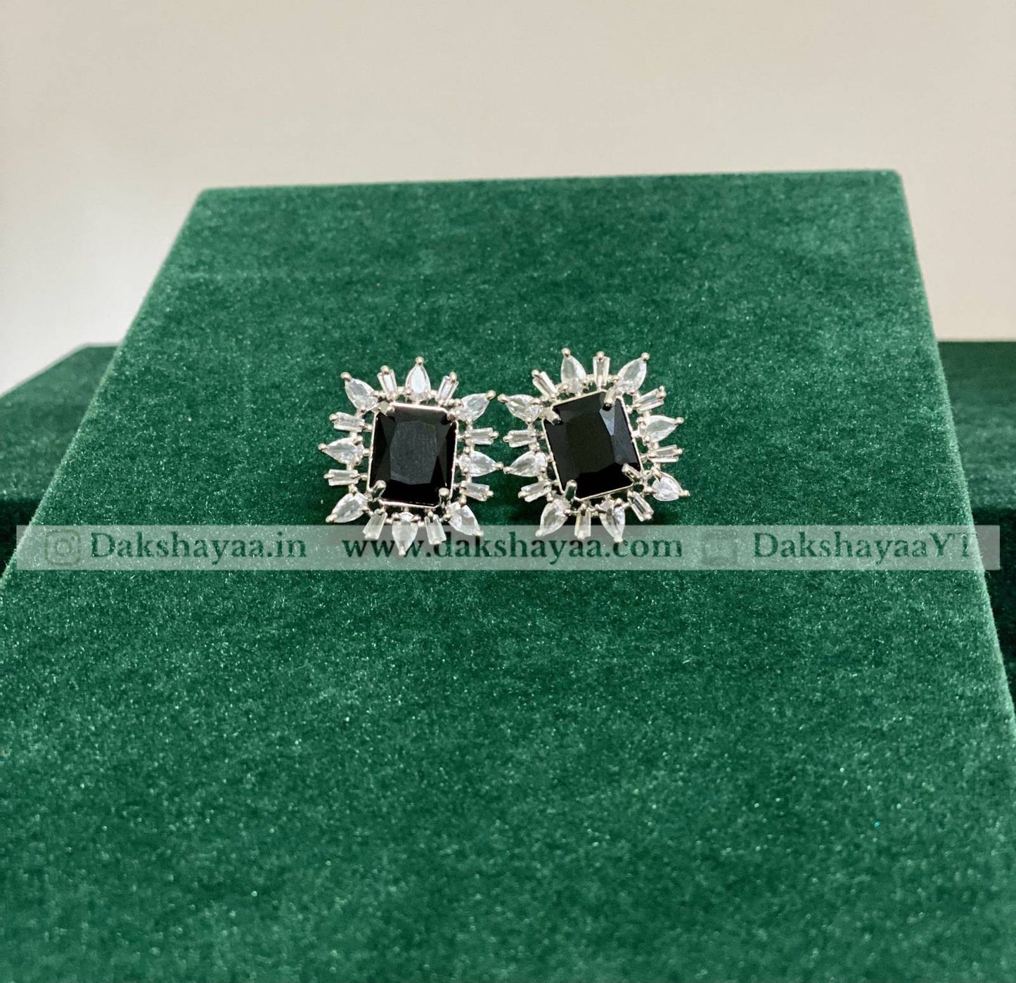 Pair of earrings with black stones and silver accents on a green cushion.