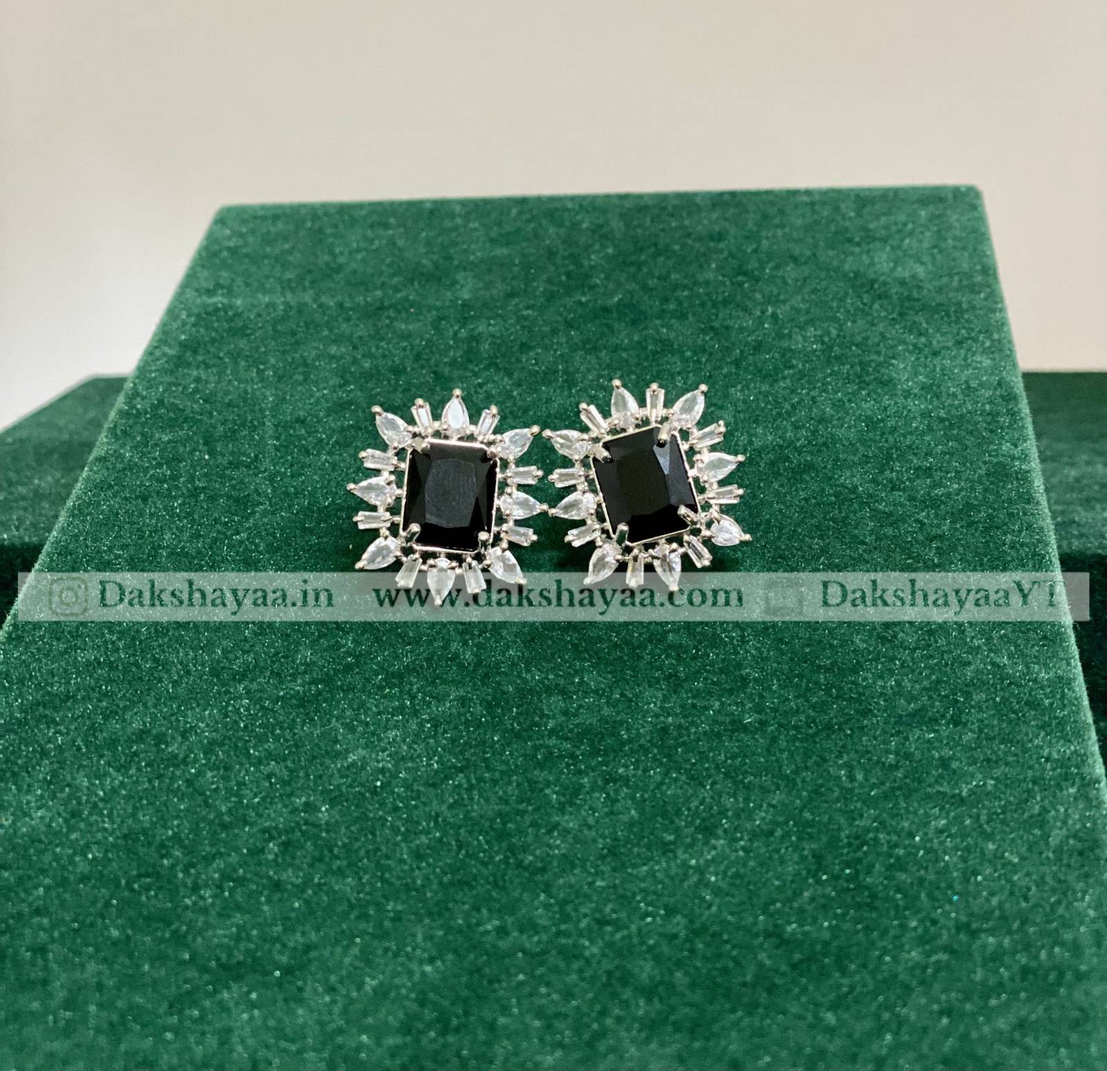 Pair of earrings with black stones and silver accents on a green cushion.
