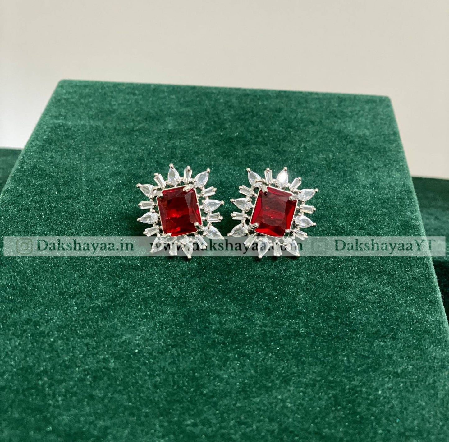 Silver earrings with red gemstones on a green cushion