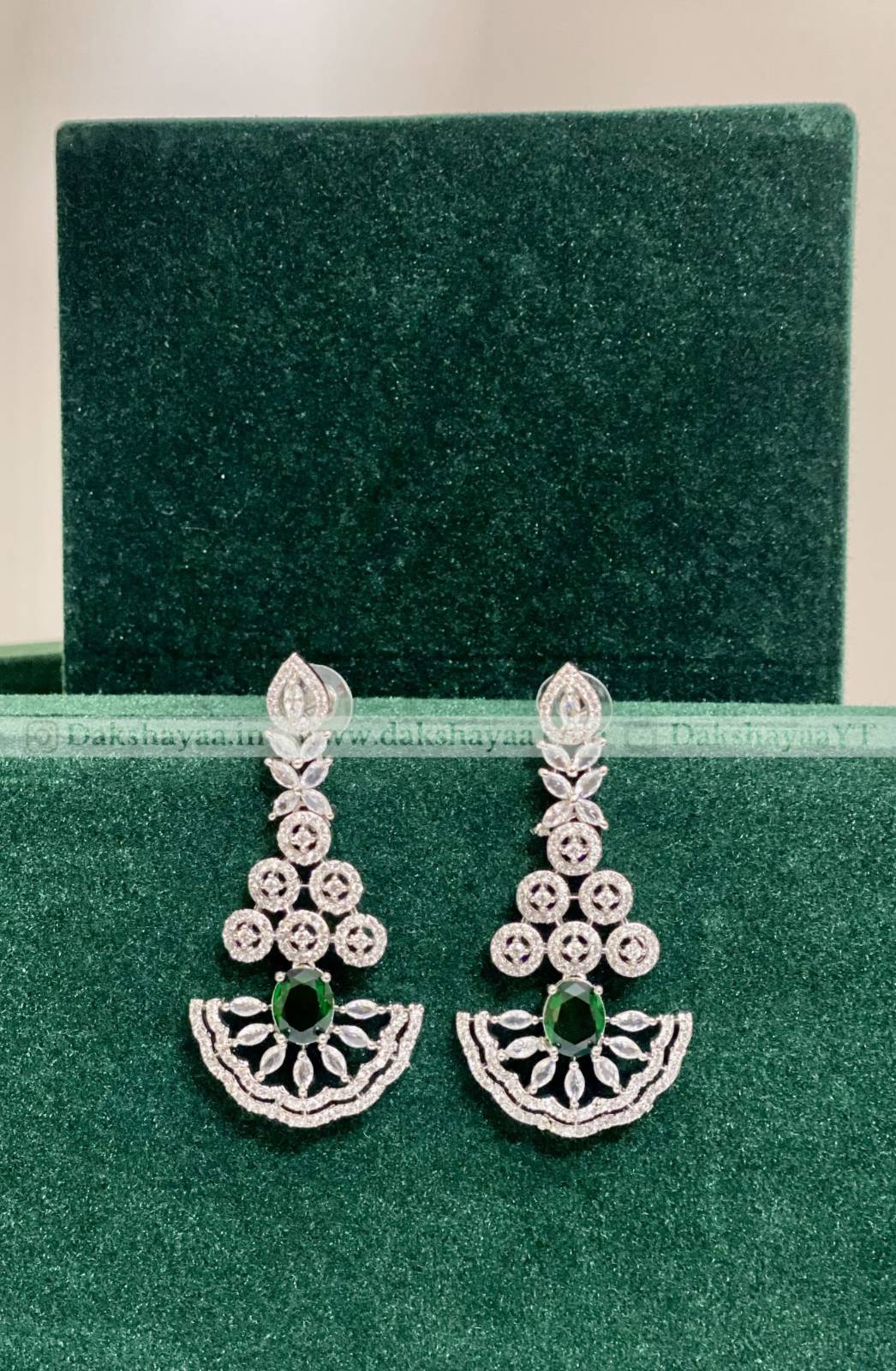 Pair of silver earrings with green gemstones on a green velvet background