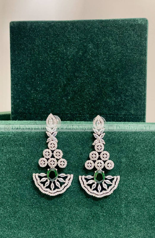 Pair of silver earrings with green gemstones on a green velvet background