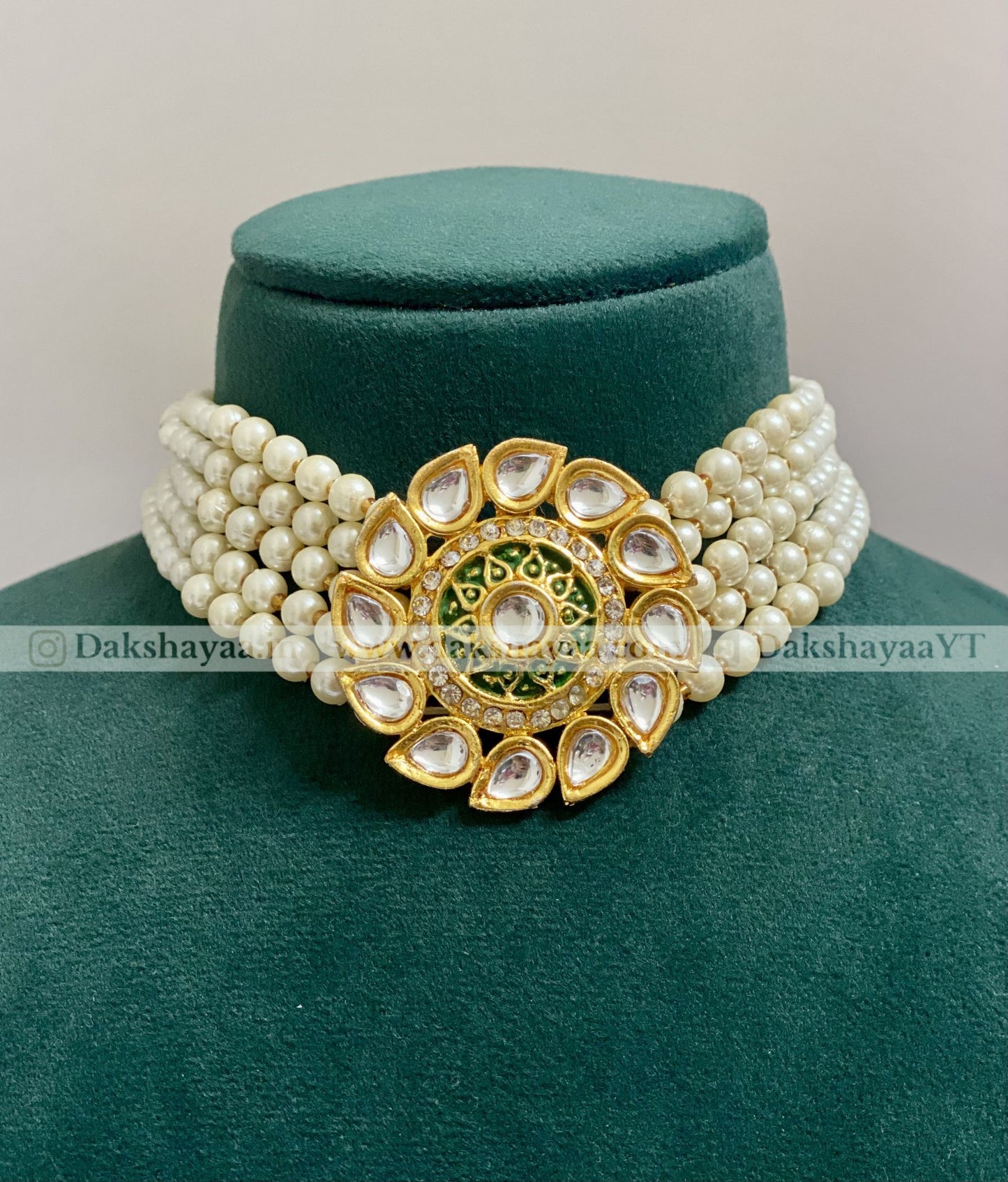 Pearl necklace with a gold and green decorative clasp on a green velvet stand.