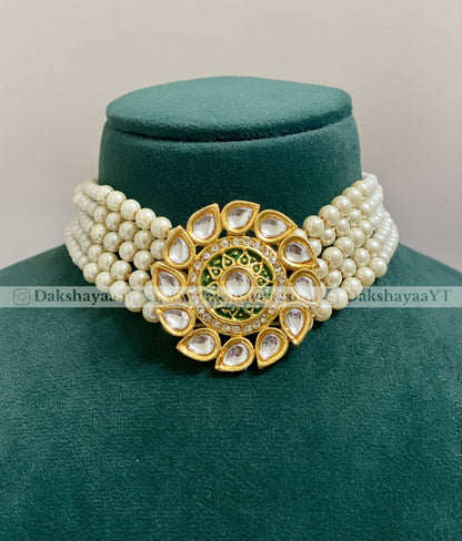 Pearl necklace with a gold and green decorative clasp on a green velvet stand.
