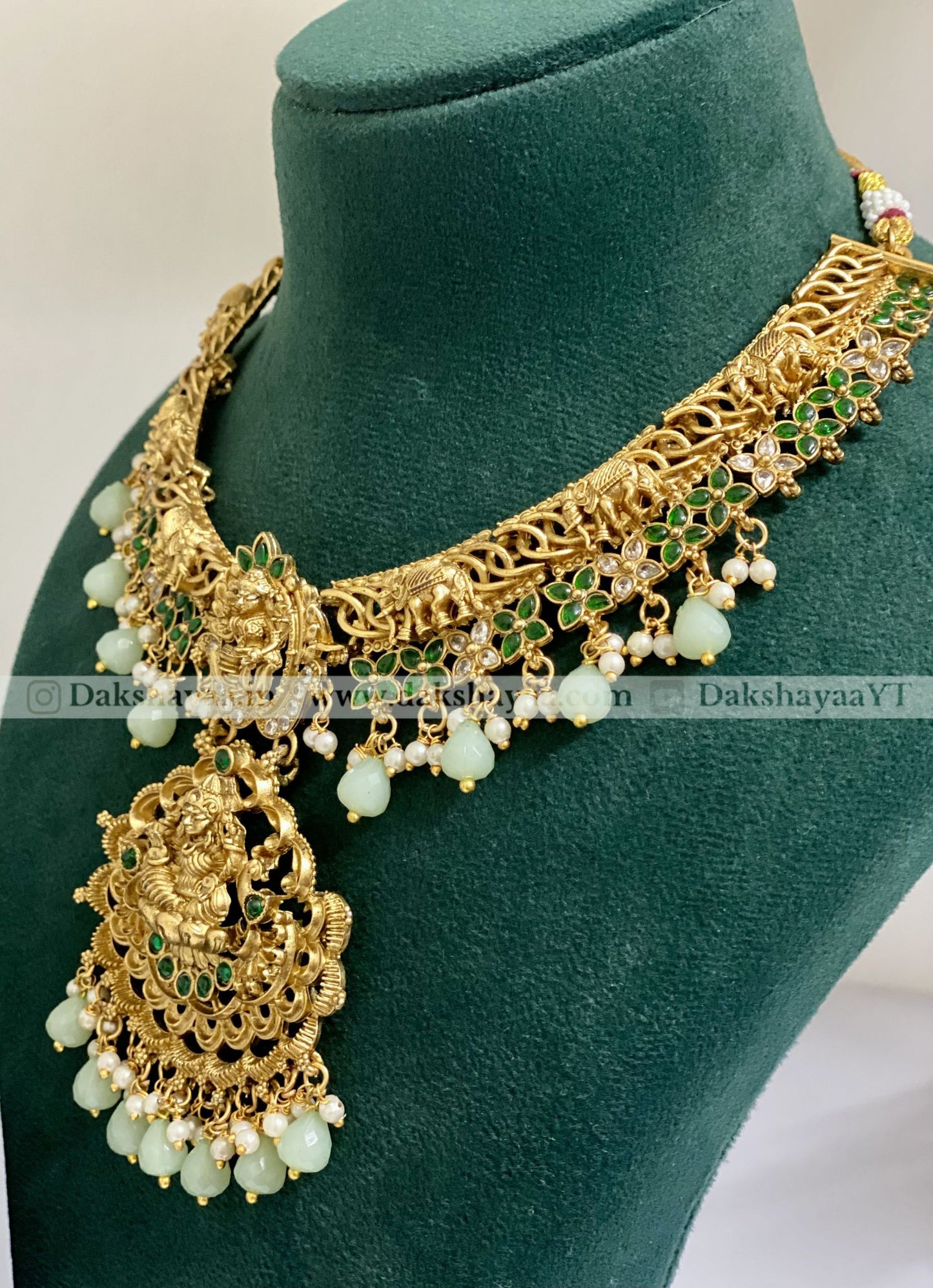 Gold necklace with green and white stones on a green mannequin