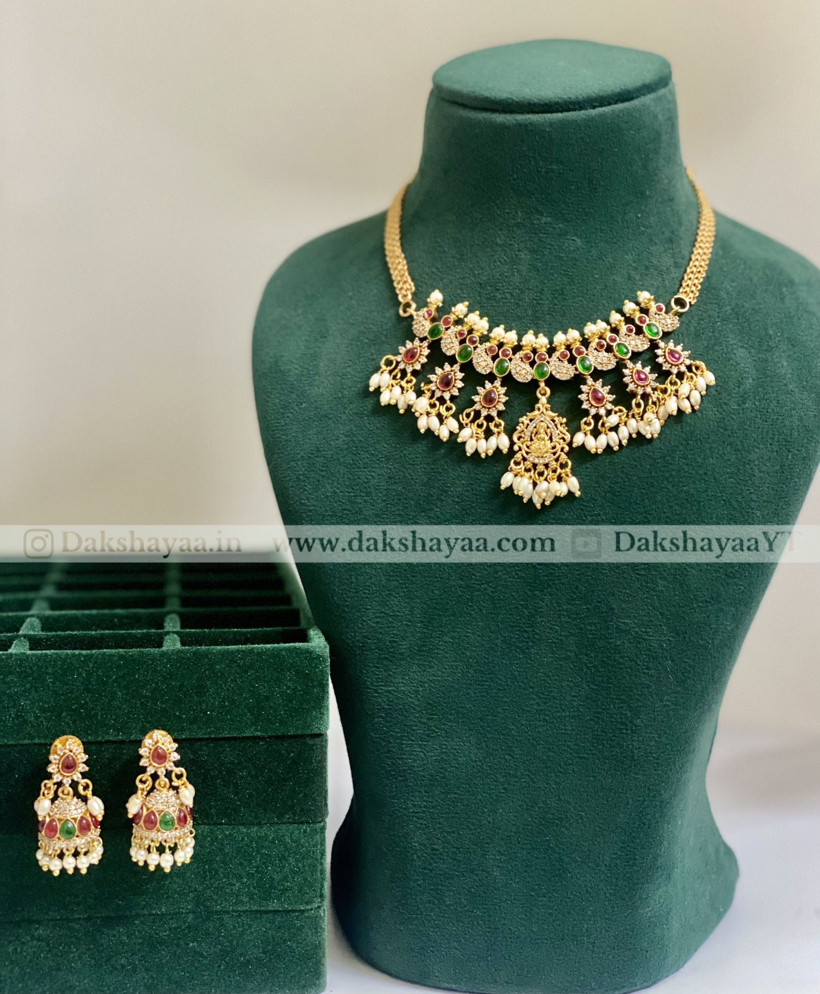Gold necklace and earrings on a green mannequin with a green box in the background