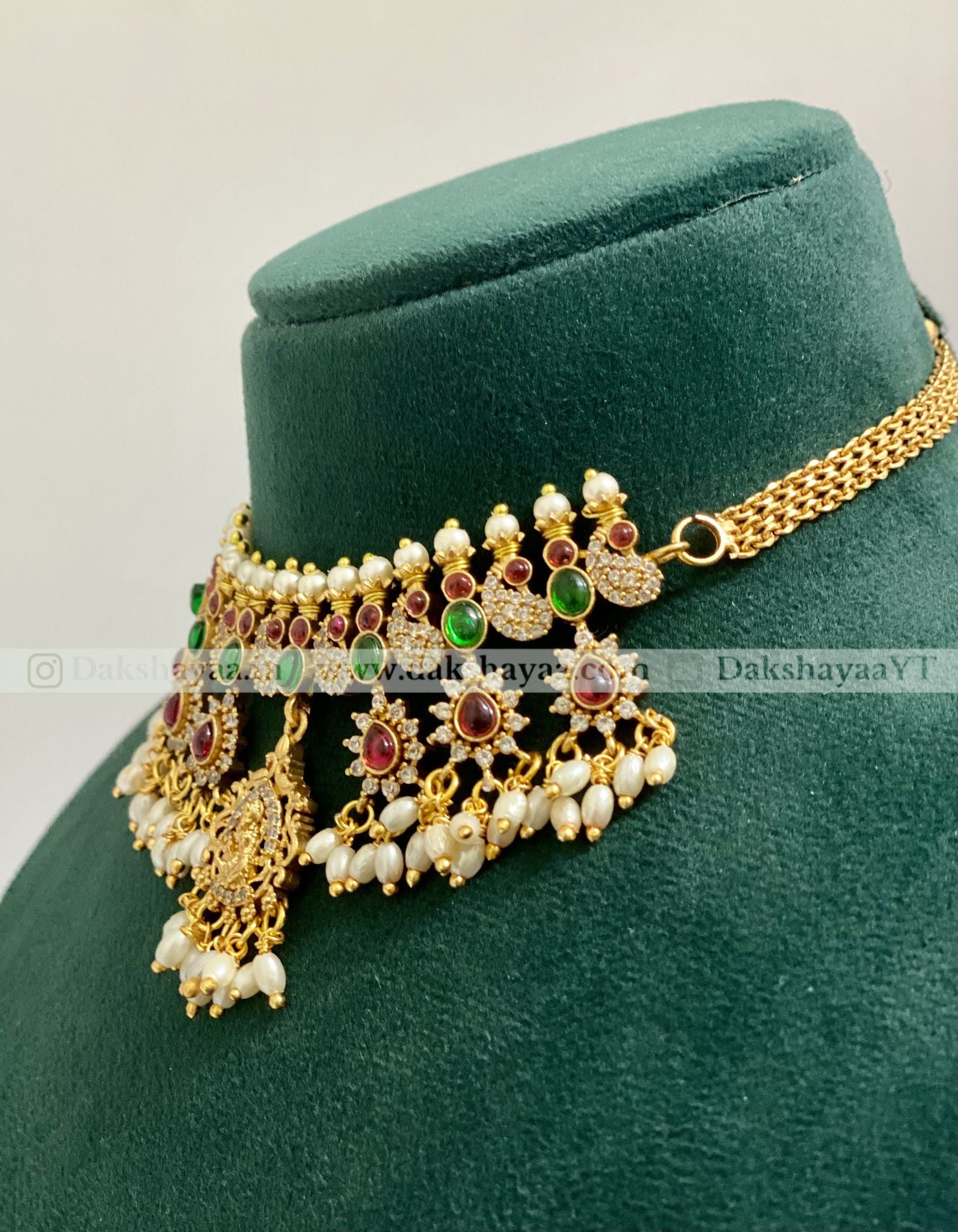 Gold necklace with green and red stones on a green velvet stand