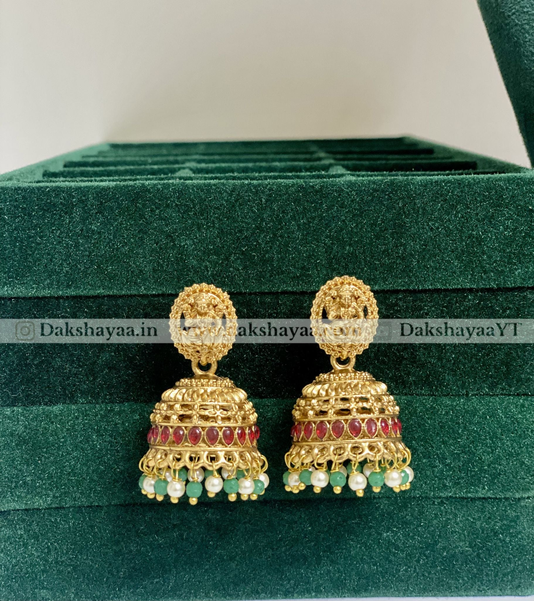 Gold earrings with red and green stones on a green velvet surface