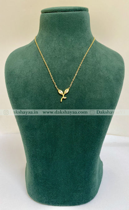 Gold necklace with a leaf pendant on a green mannequin bust, brand 'Dakshayaa' visible.