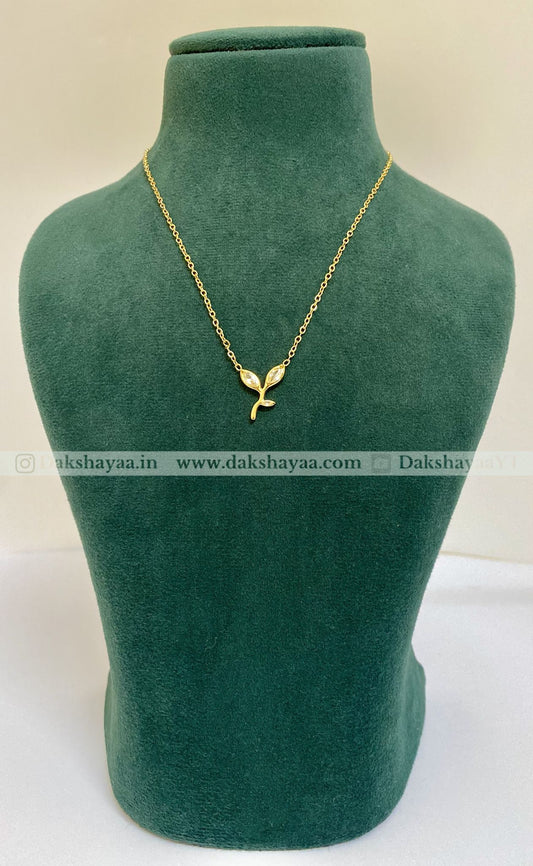 Gold necklace with a leaf pendant on a green mannequin bust, brand 'Dakshayaa' visible.
