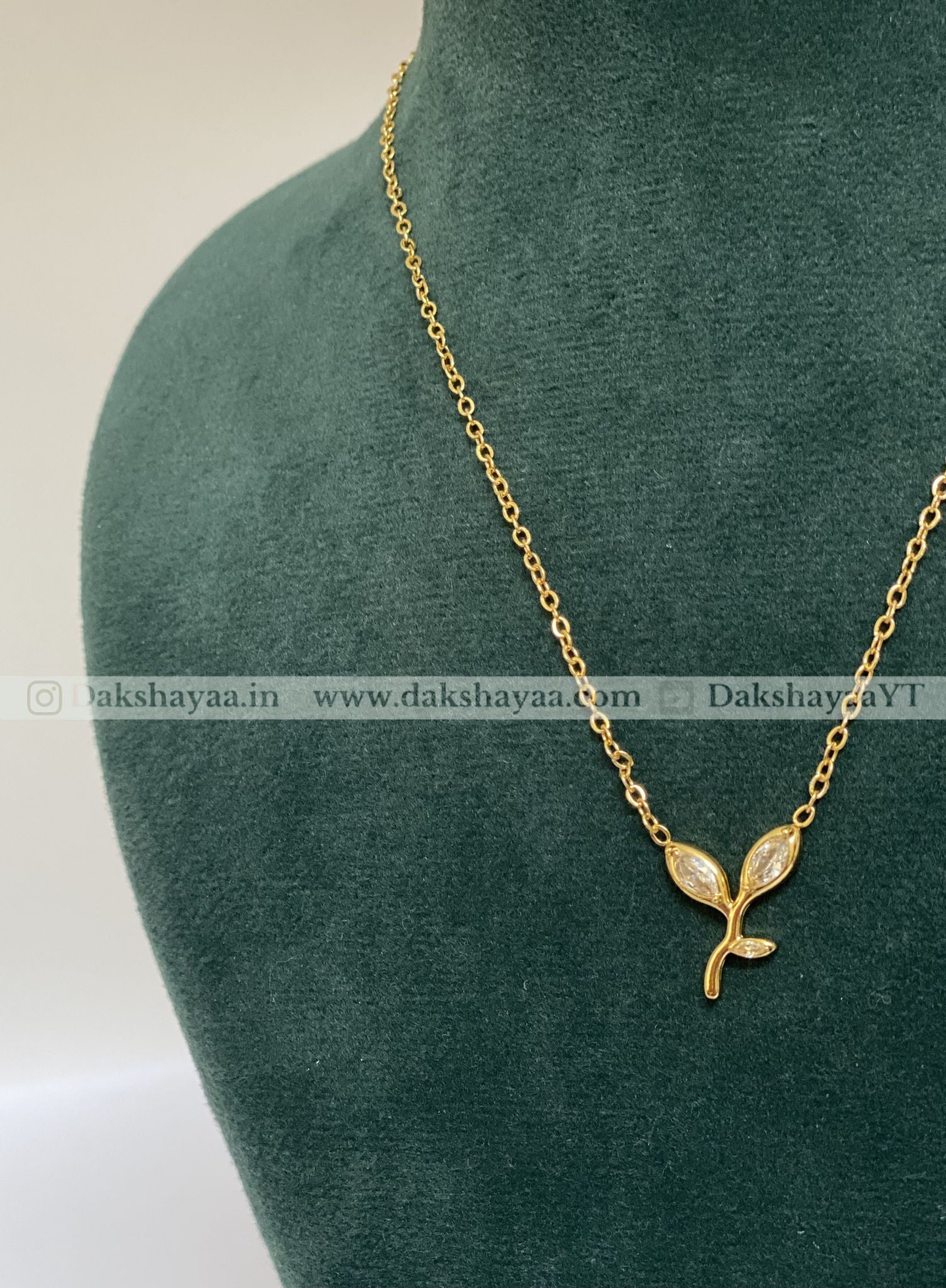 Gold necklace with a leaf pendant on a green mannequin