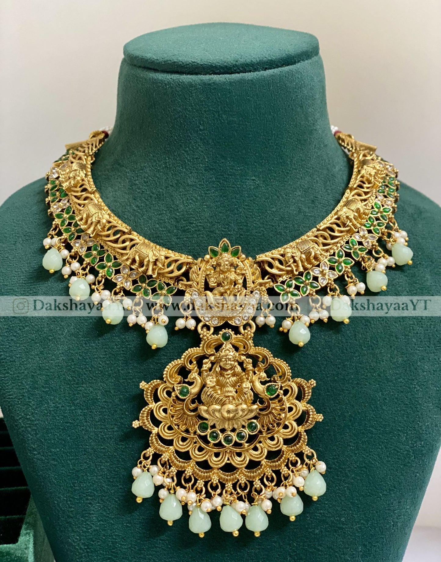 Ornate gold necklace with green and white beads on a green mannequin