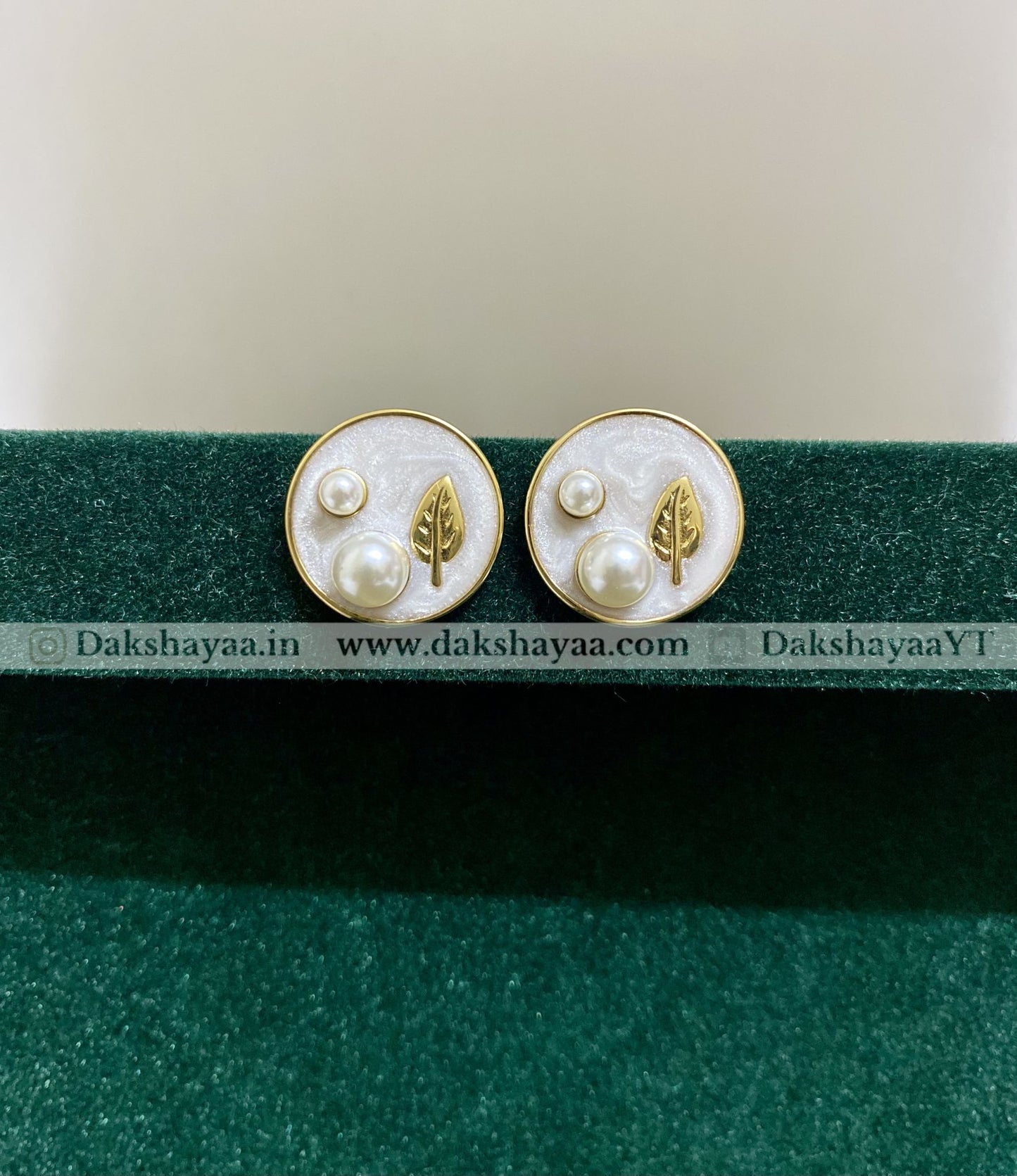 Pair of earrings with leaf and pearl design on a green stand with visible branding.
