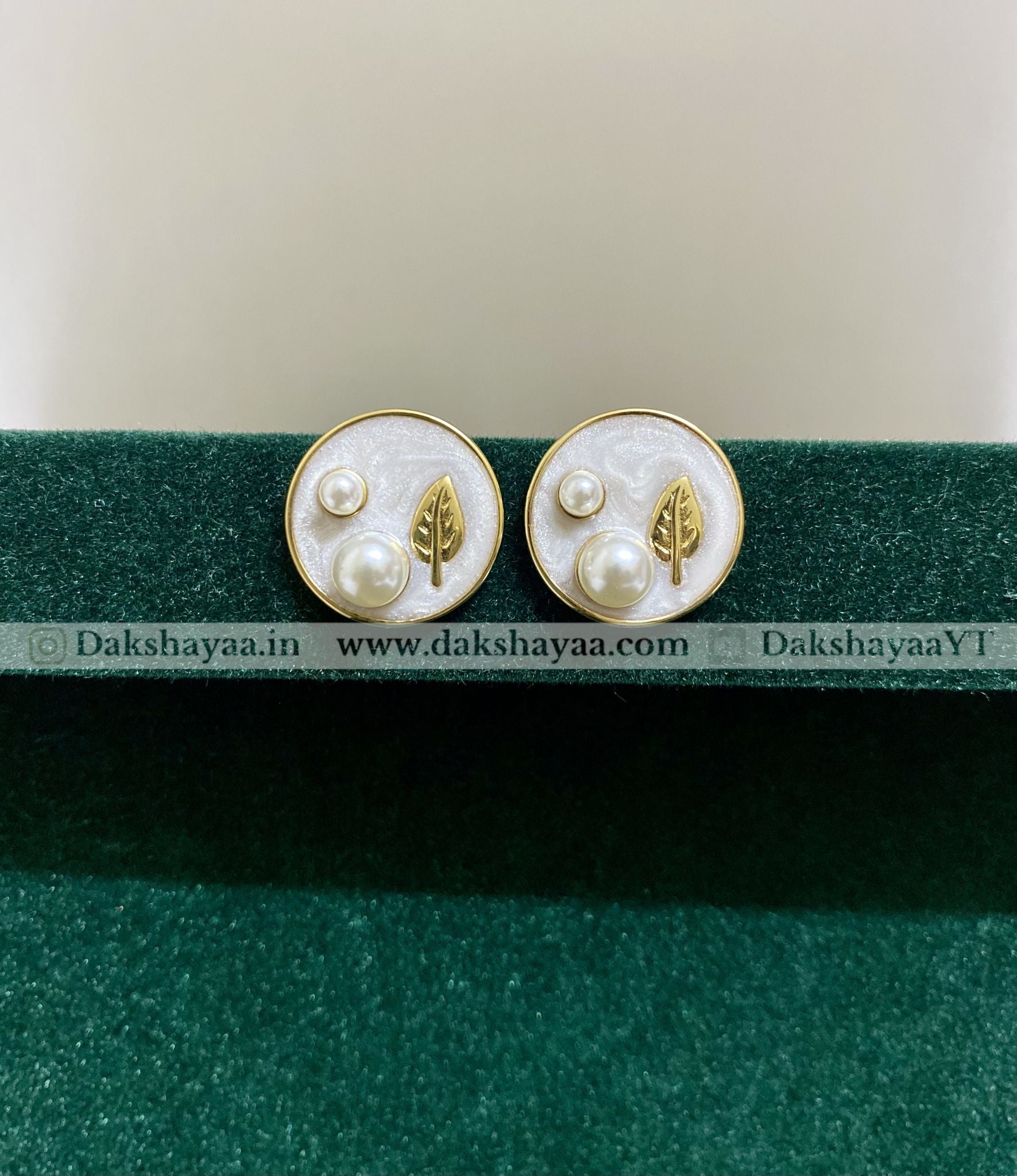 Pair of earrings with leaf and pearl design on a green stand with visible branding.