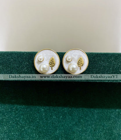 Pair of earrings with leaf and pearl design on a green stand with visible branding.