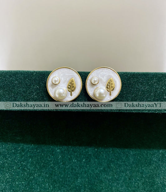 Pair of earrings with leaf and pearl design on a green stand with visible branding.