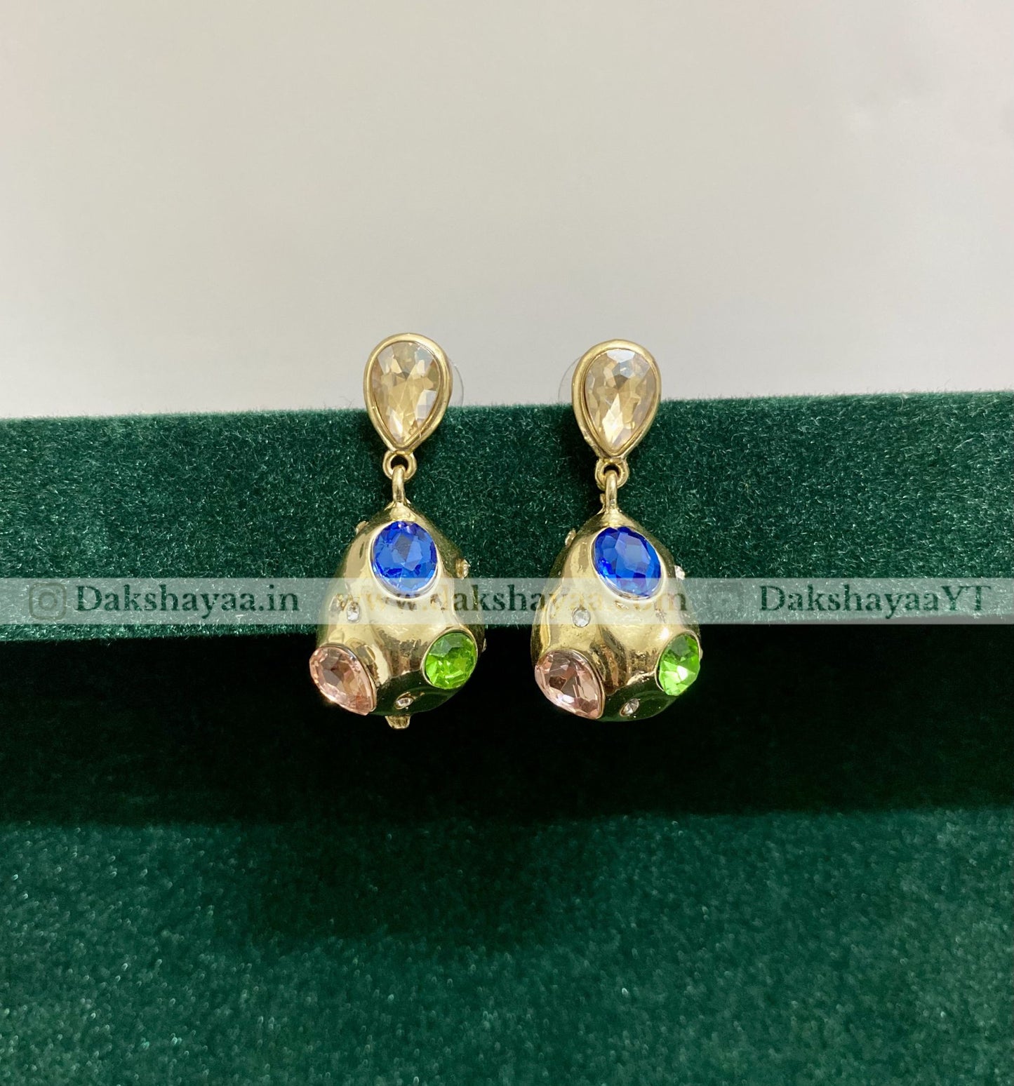 Pair of gold earrings with gemstones on a green background