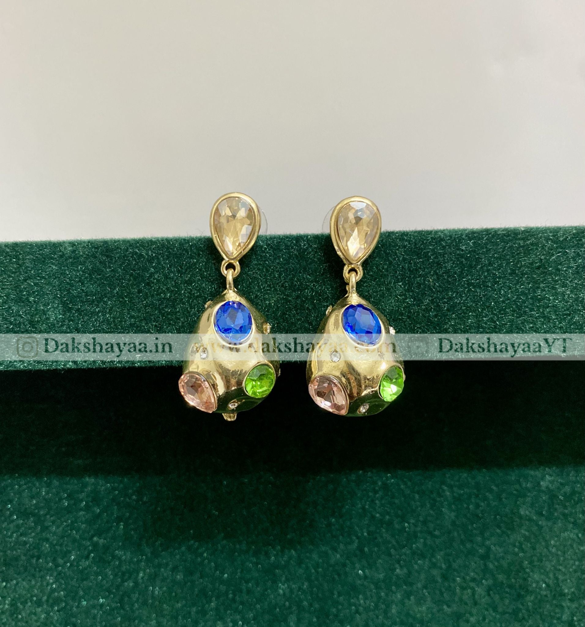 Pair of gold earrings with gemstones on a green background