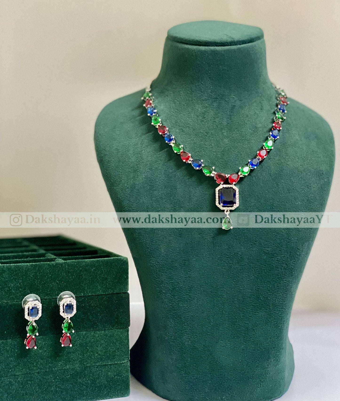 Colorful necklace and earrings on a green mannequin with a branded box in the background.