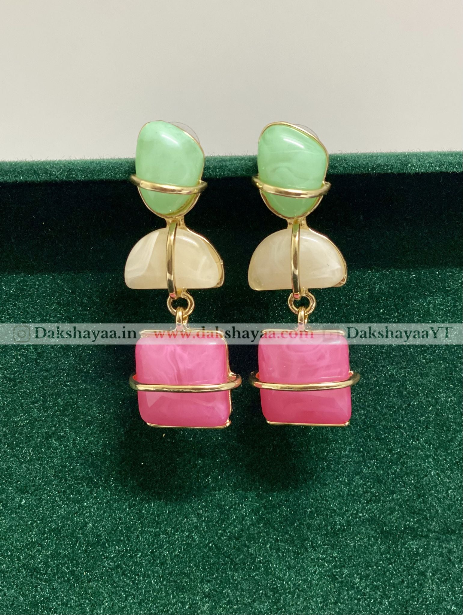 Pair of earrings with green and pink stones on a green background