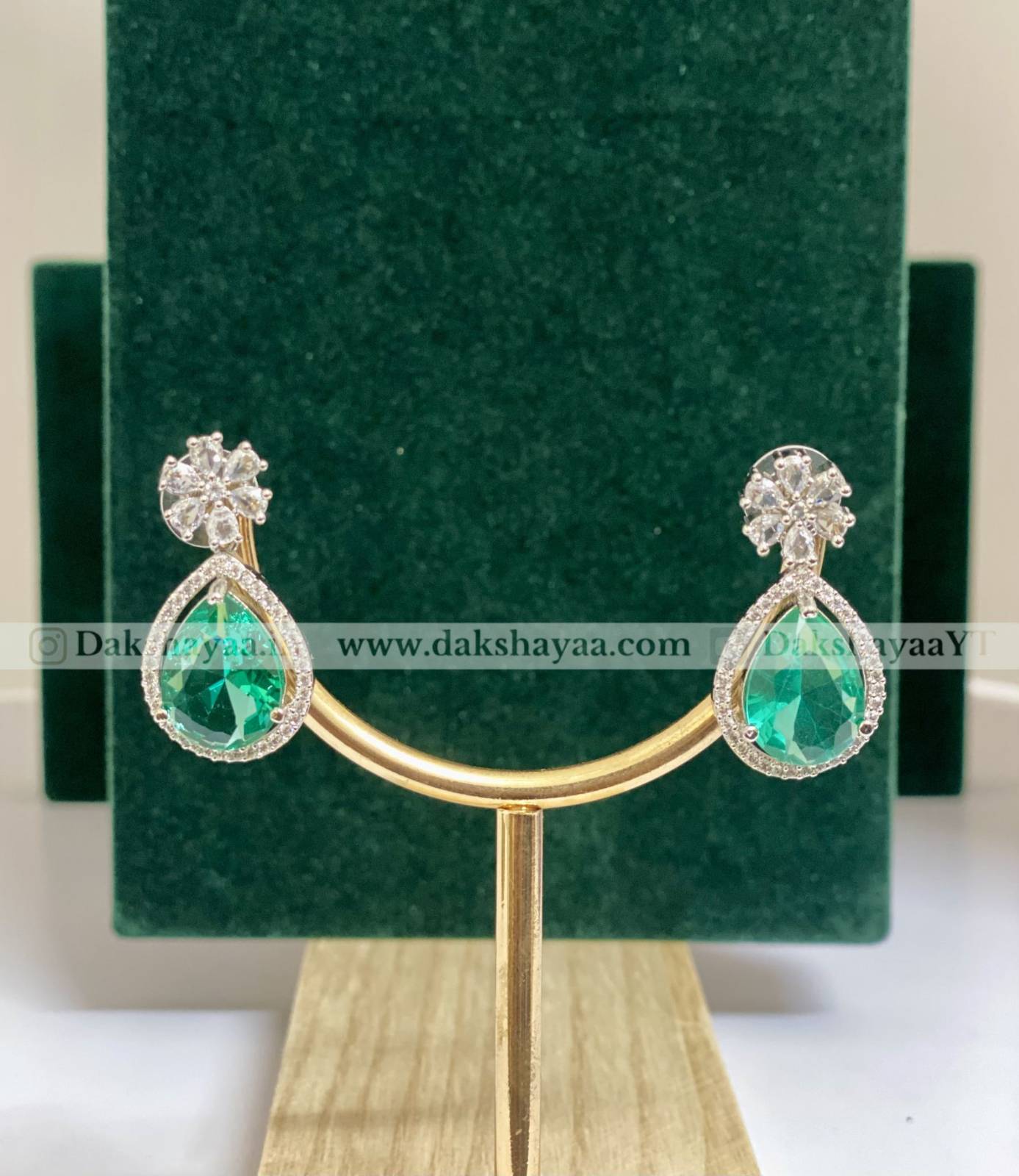 Pair of emerald green teardrop earrings on a gold stand with a green velvet background.