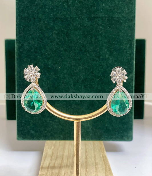 Pair of emerald green teardrop earrings on a gold stand with a green velvet background.