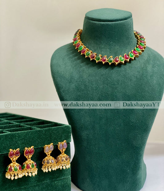 Gold necklace with red and green gemstones on a green mannequin bust, next to matching earrings in a green box.
