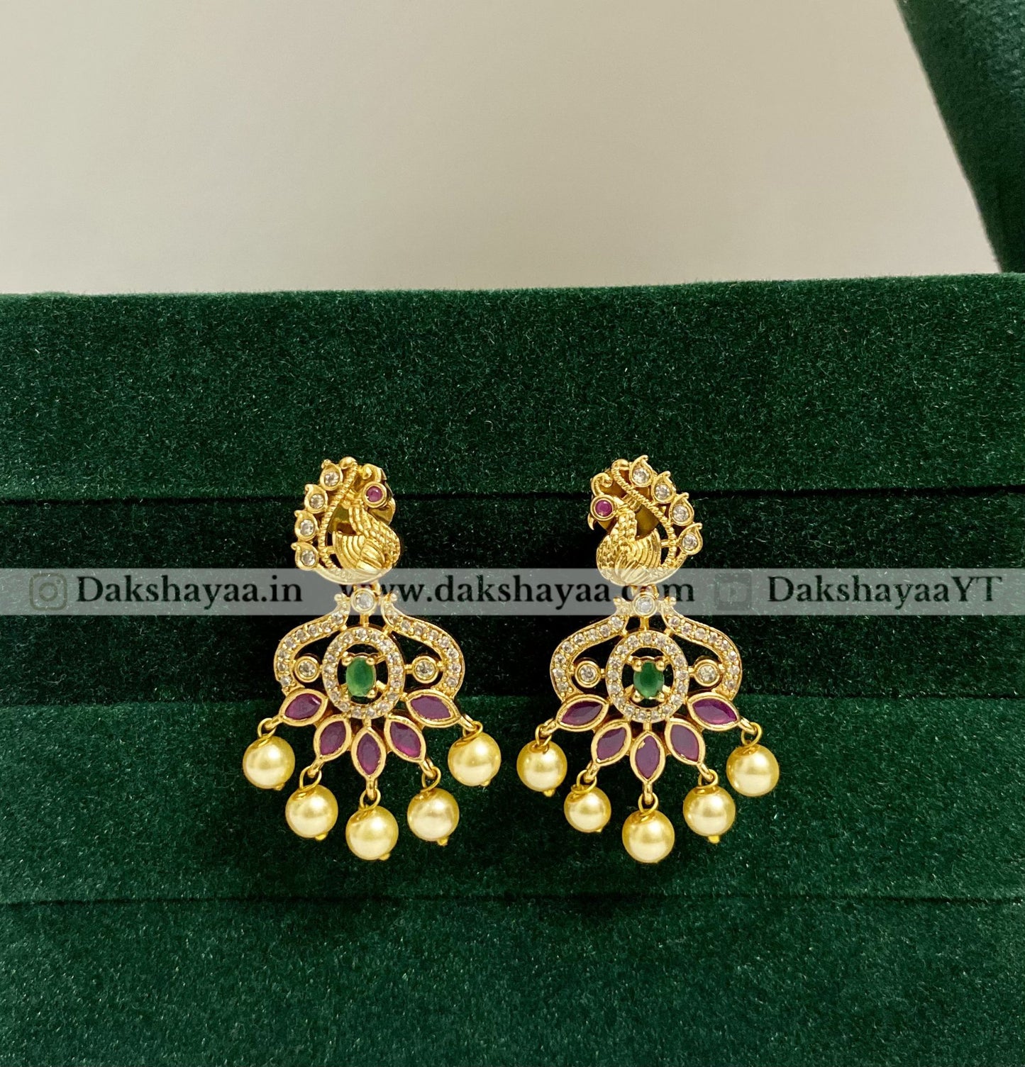 Gold earrings with green and red stones on a green velvet background
