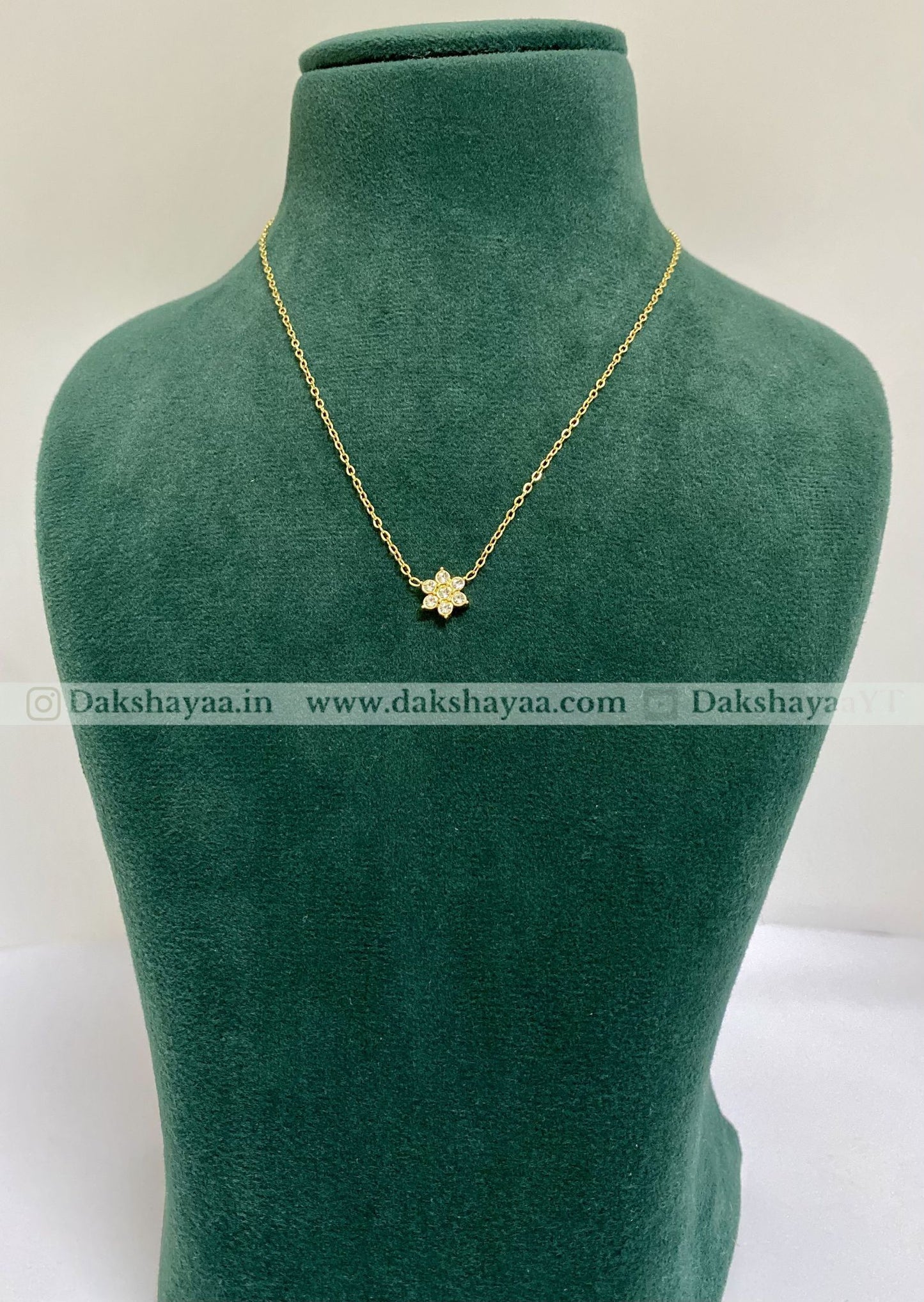 Gold necklace with a star pendant on a green mannequin bust, brand 'Dakshayaa' visible.